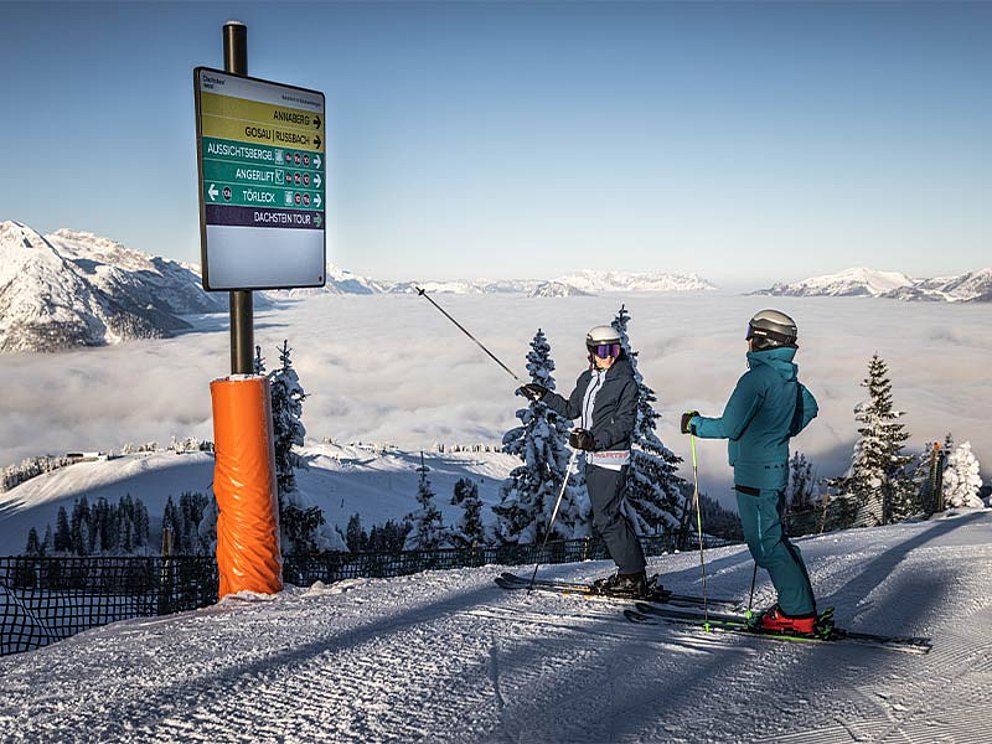 2 Skifahrer vor einer Wegweisertafel auf der Piste