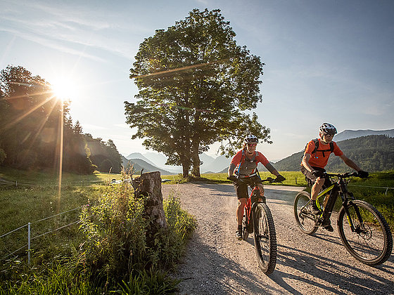 2 Biker beim Sonnenuntergang auf einem ebenen Schotterweg