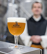 Ein Glas Bier mit schöner Schaumkrone, im Hintergrund ein Mönch