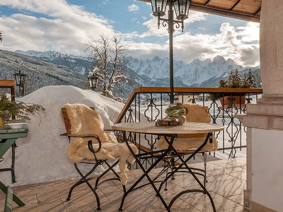 ein Tisch und 2 Sessel auf der winterlichen Terrasse mit Schneebergen im Hintergrund