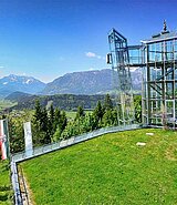 Außenansicht vom gläsernen Panoramaturm, im Hintergrund Bergkulisse