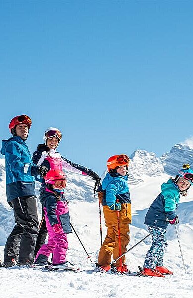 Eltern mit 2 Kindern auf Skiern vor dem Dachstein-Massiv